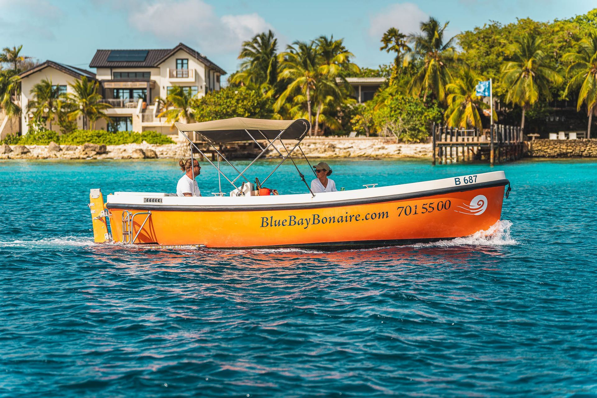 Blue Bay Boot verhuur Bonaire oranje sloep vaart rustig over het lichtblauwe water bij de kust van Bonaire.