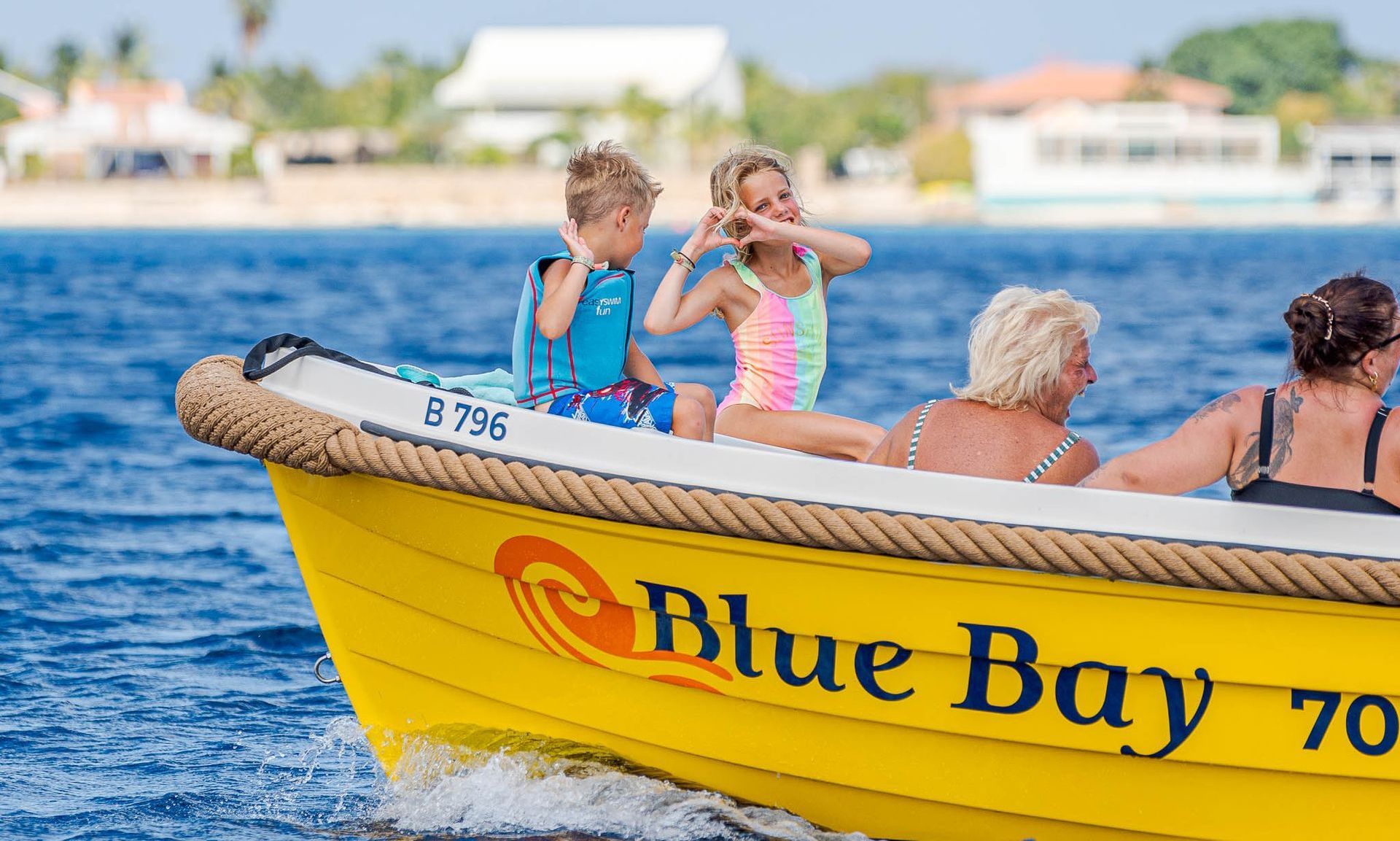 Blue Bay Bonaire Yellow Sloop on the water, two kids in the front are smiling to the camera.