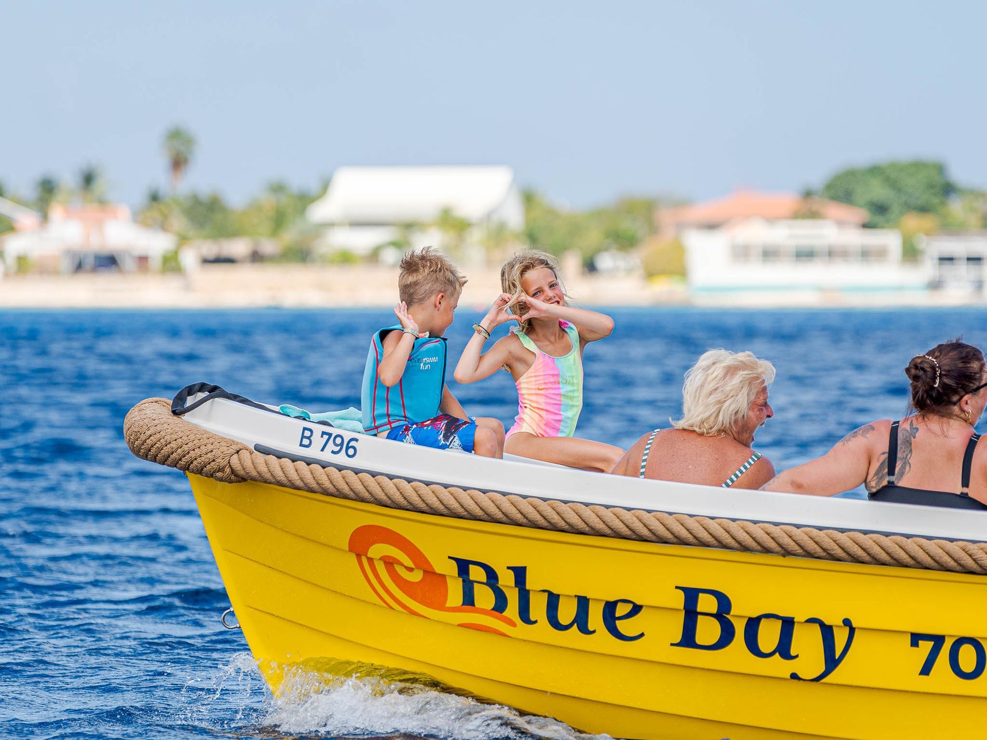 Blue Bay Bonaire Boat Rental Yellow sloep with 2 kids in the front making a heart to the camera