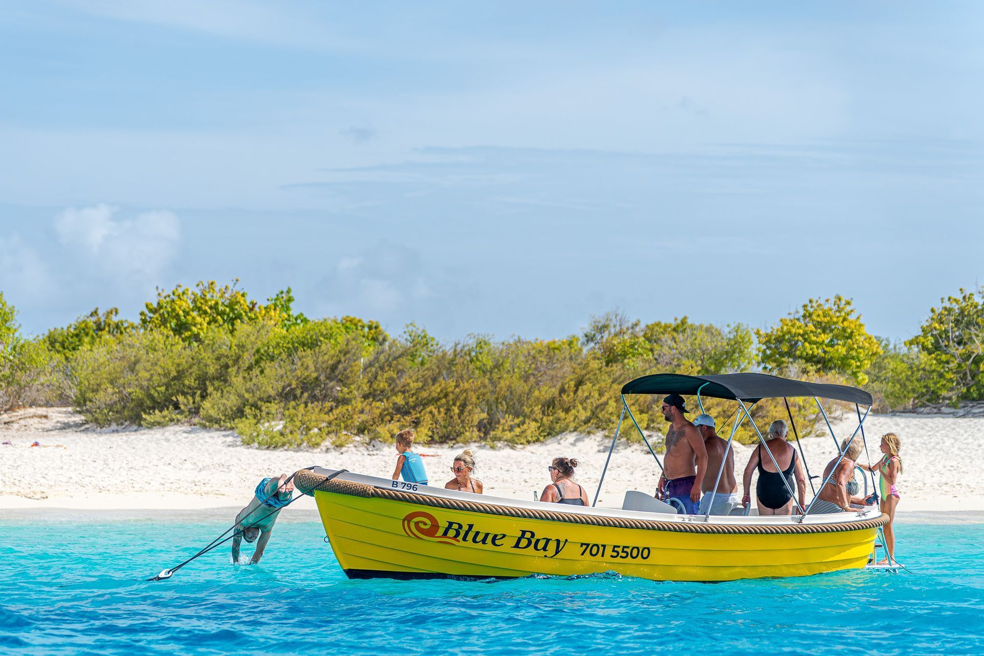 Blue Motor Boat Rental lying in light blue Caribbean Sea, three young women swimming and snorkling.