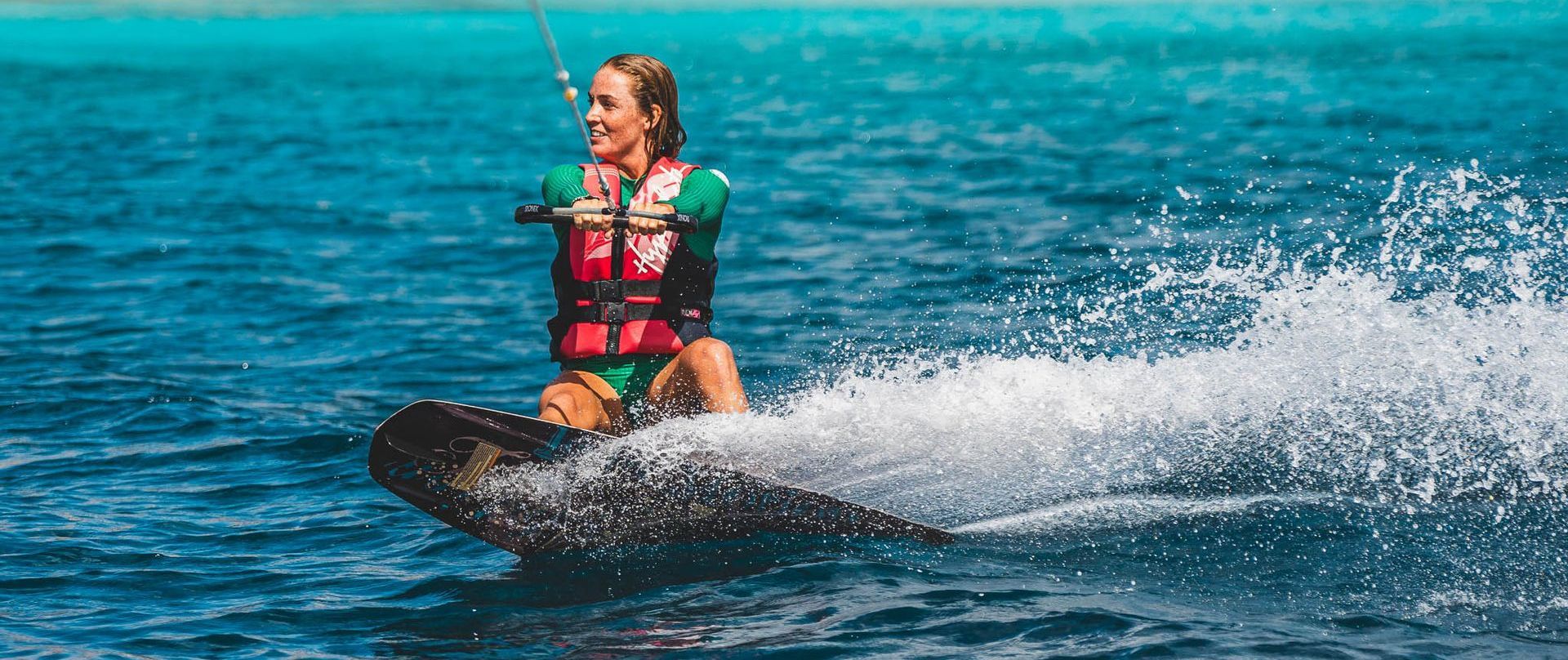 Blue Bay Bonaire Boat Rental young woman in green surfsuit is wakeboarding.