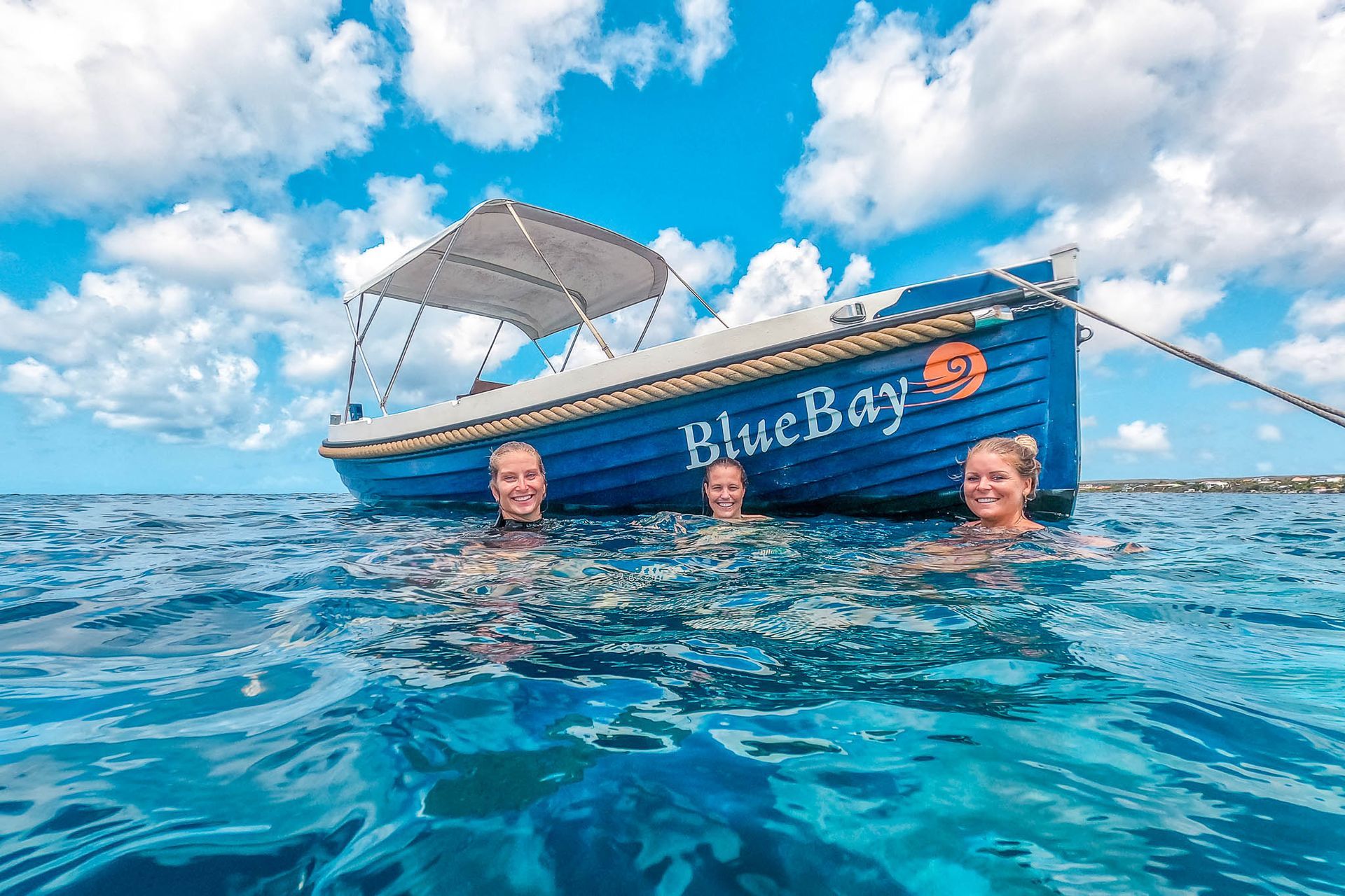 Blue Motor Boat Rental lying in light blue Caribbean Sea, three young women swimming and snorkling.