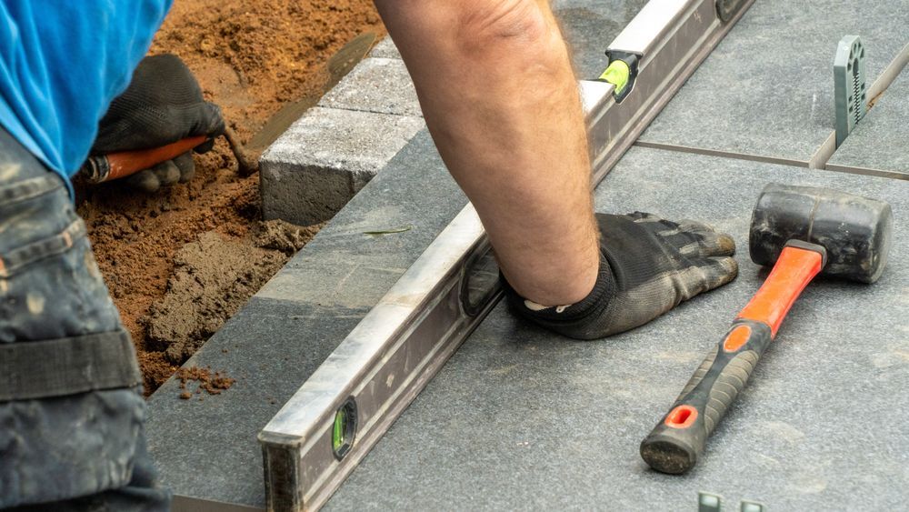 A man is using a level and a hammer to level a tile floor.