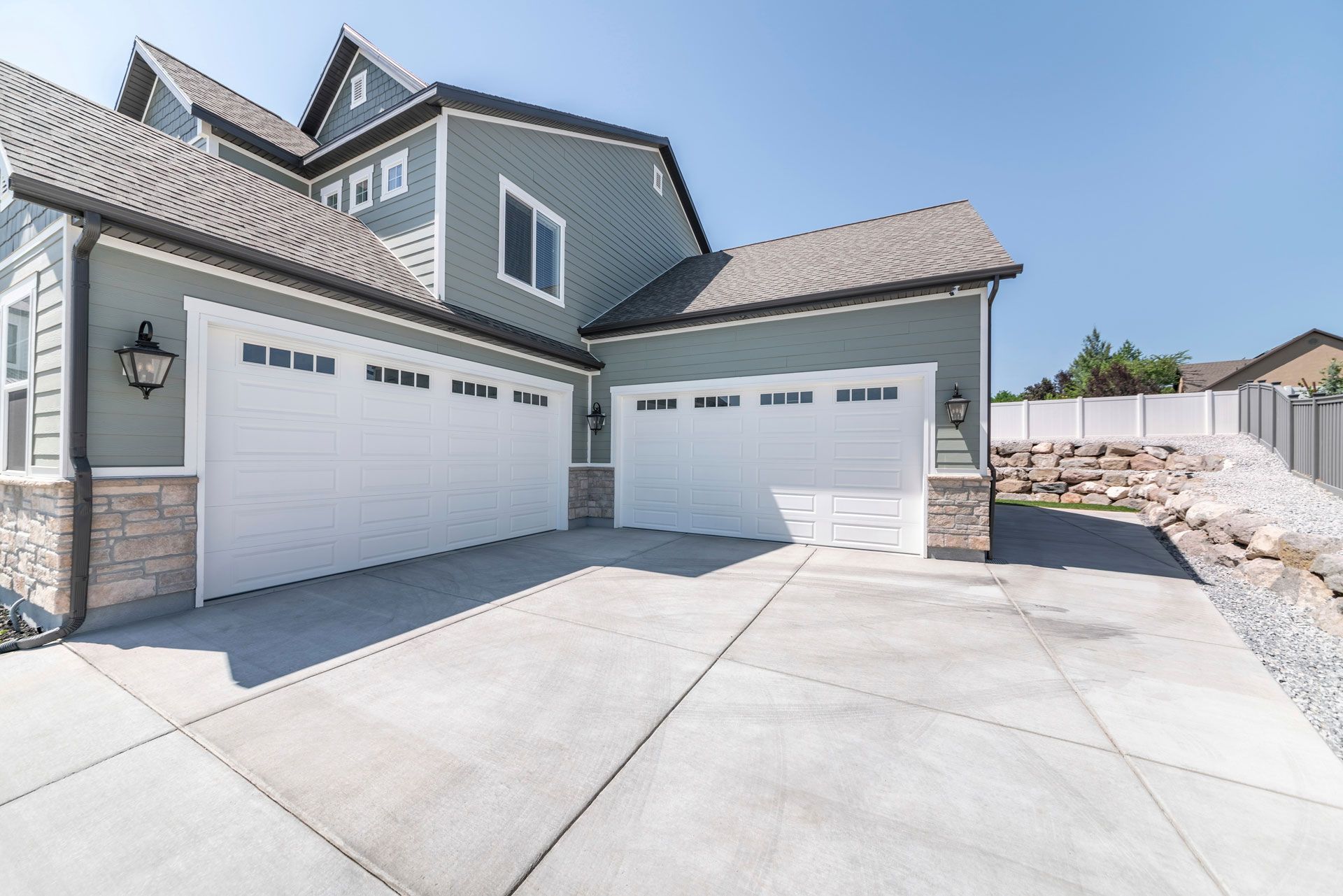 A gray two-story house with a white three-car garage and a concrete driveway on a sunny day.