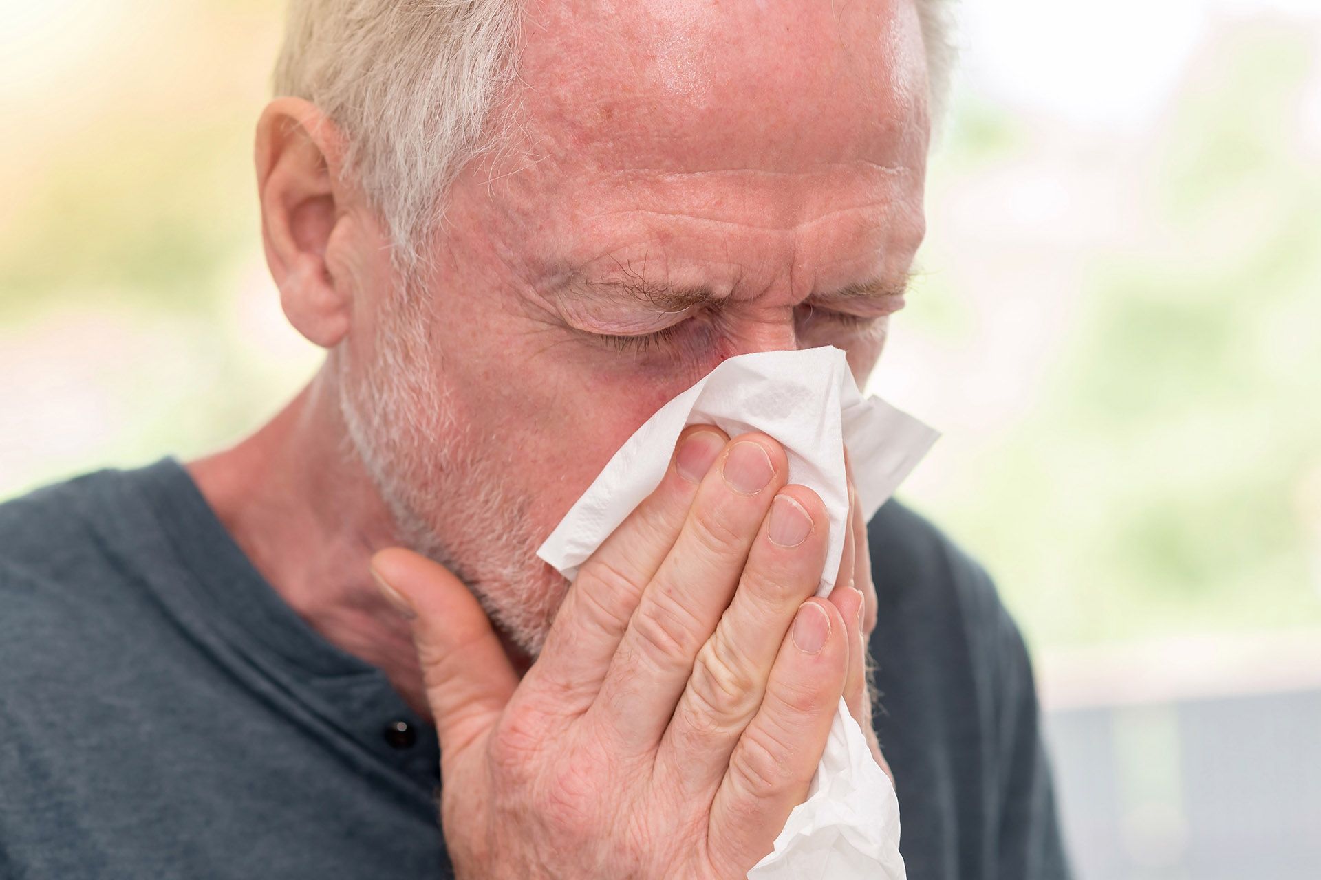 An older man is blowing his nose into a napkin.