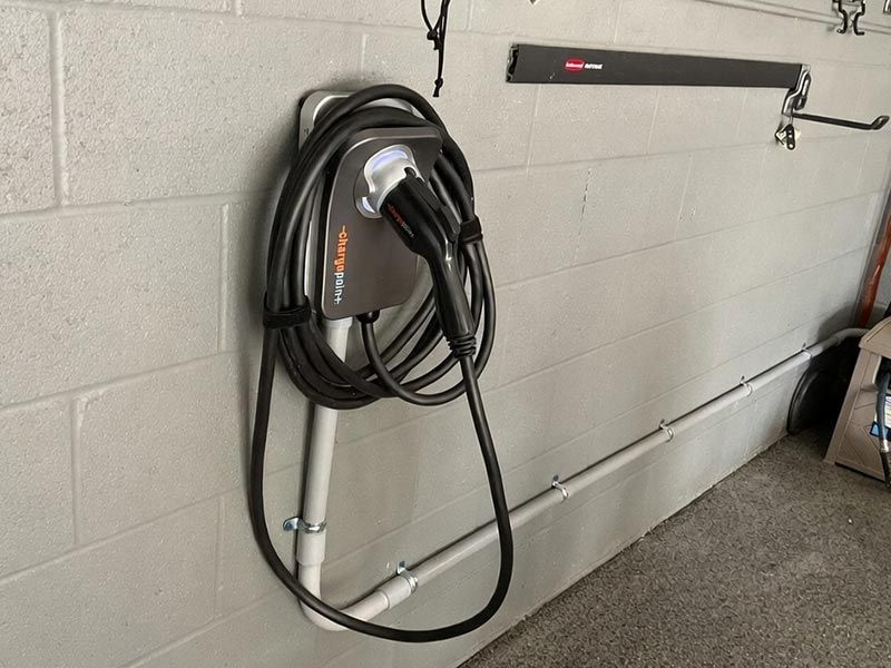 A wall-mounted ChargePoint EV charging station with a coiled black cable attached to a concrete garage wall.