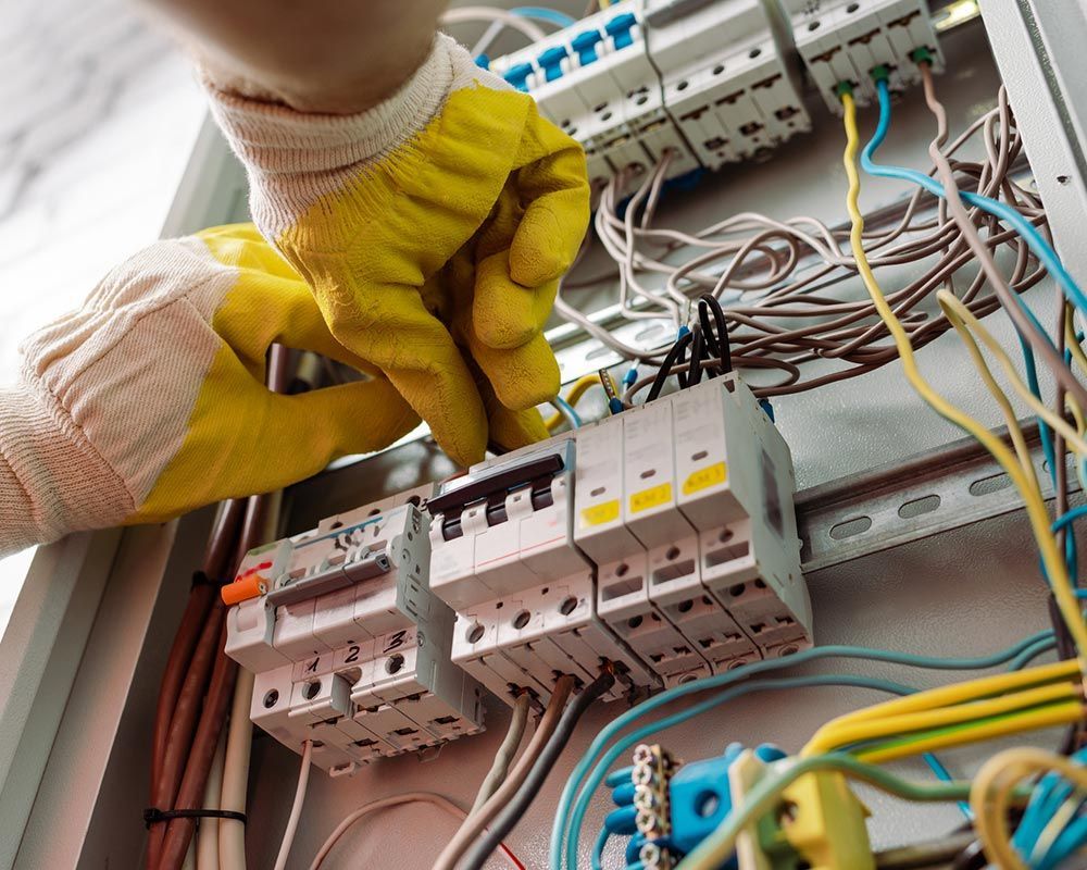 A person wearing yellow gloves is working on an electrical box