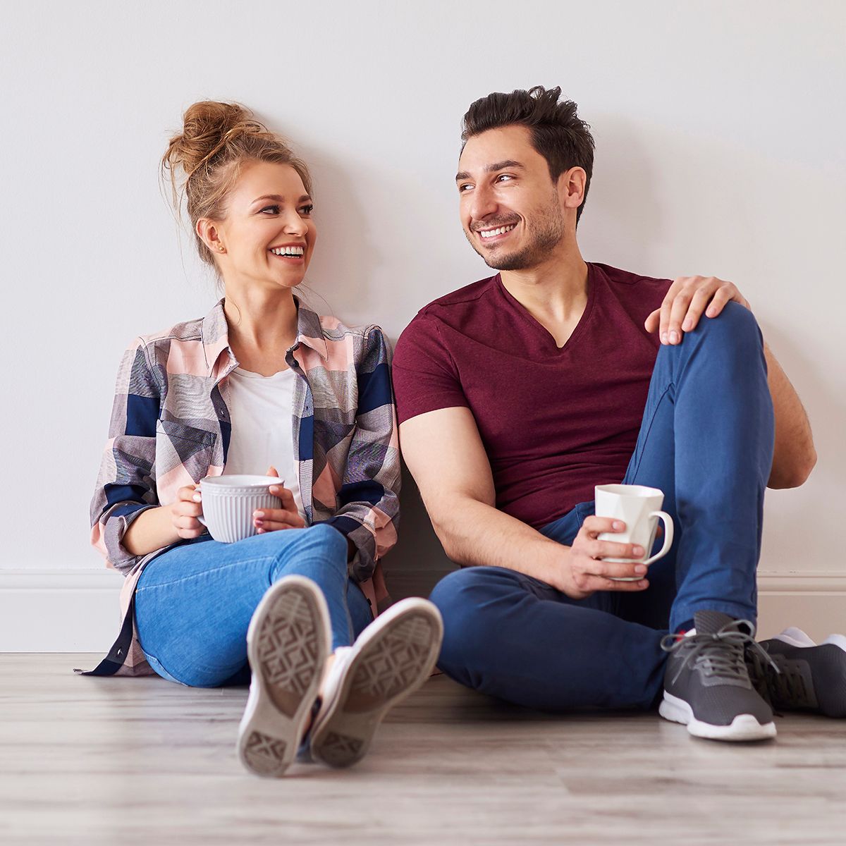 A man and a woman are sitting on the floor drinking coffee.