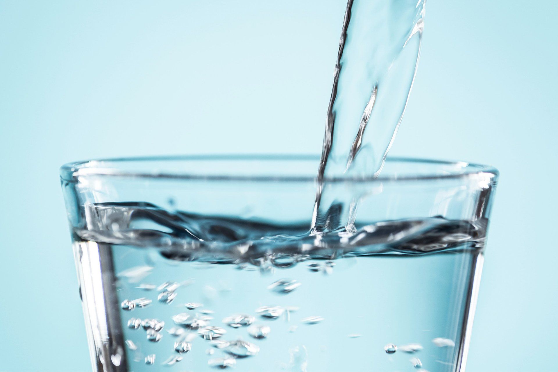 Water is being poured into a glass on a blue background.