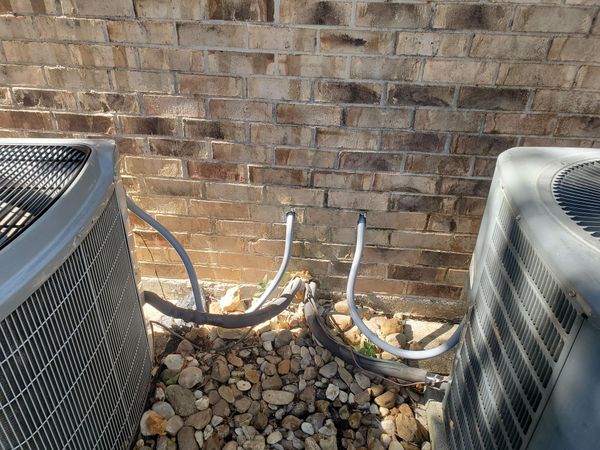 two air conditioners are sitting next to each other in front of a brick wall