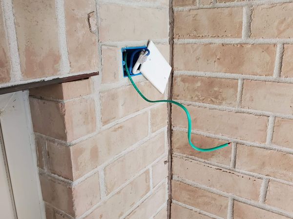 a green wire is plugged into a white box on a brick wall