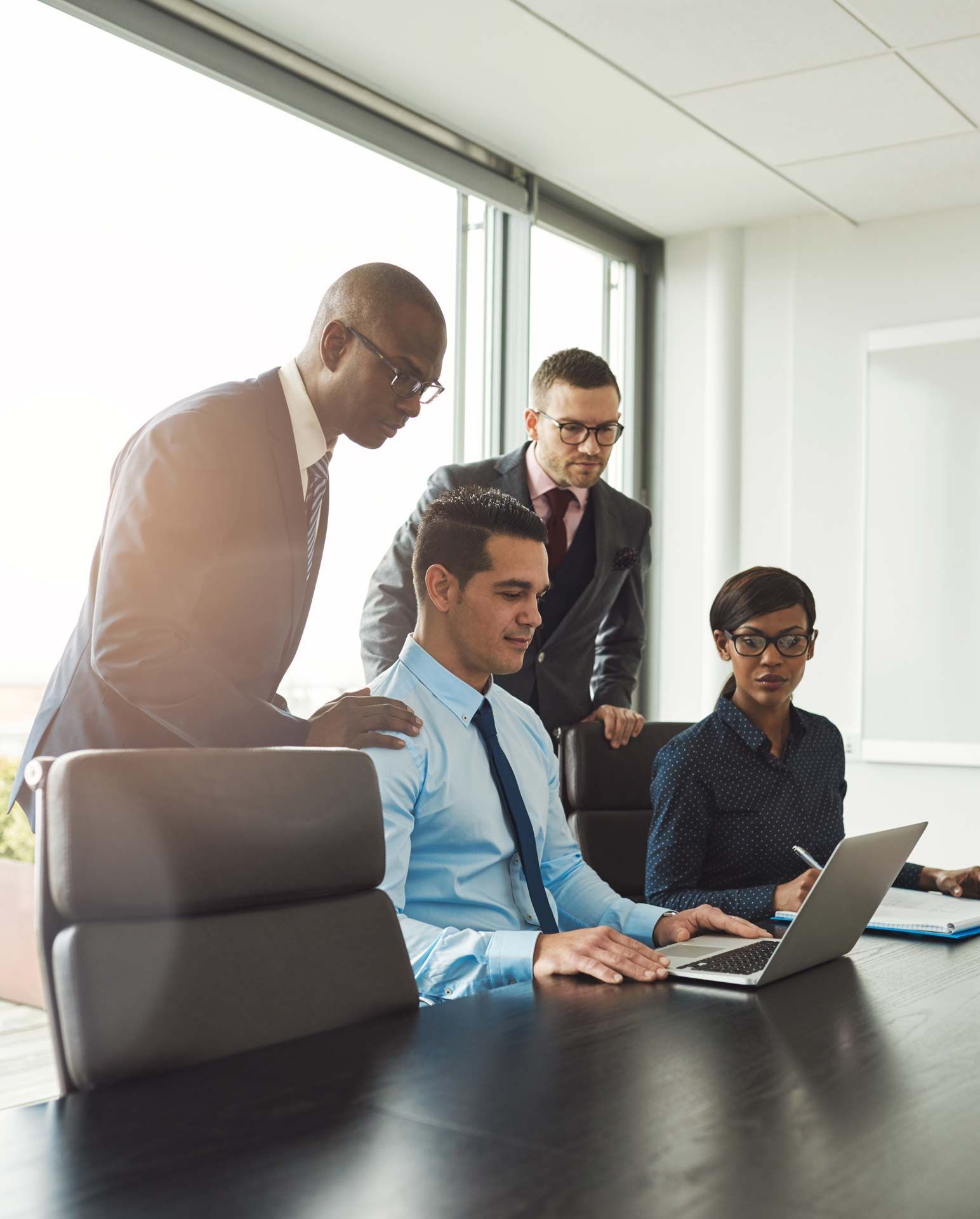 Four businesspeople collaborating around a laptop at a conference table