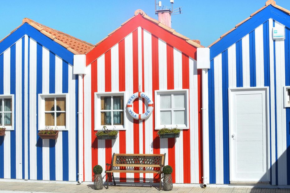 A row of red , white and blue striped houses with a bench in front of them.