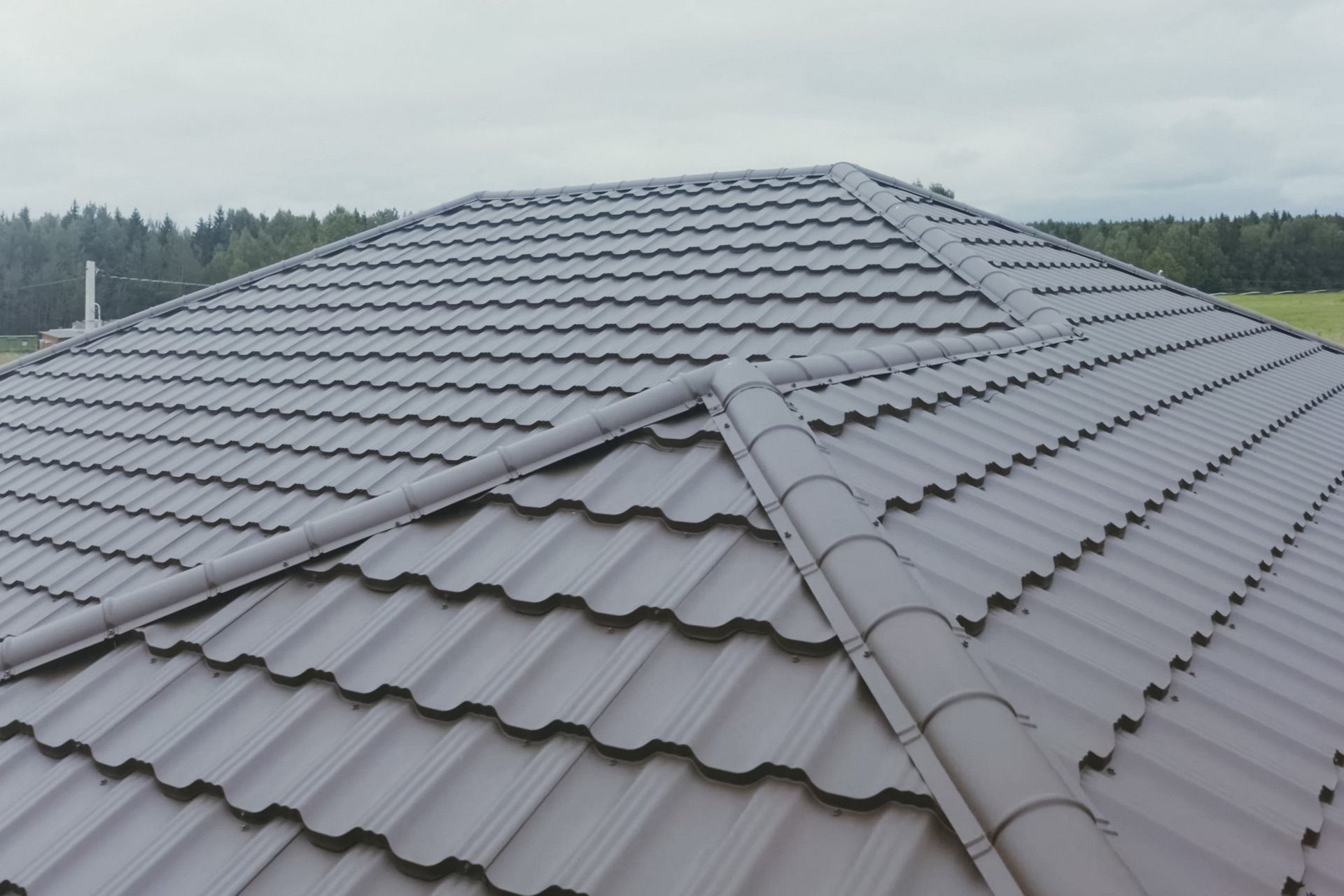 A close up of a brown tiled roof with trees in the background