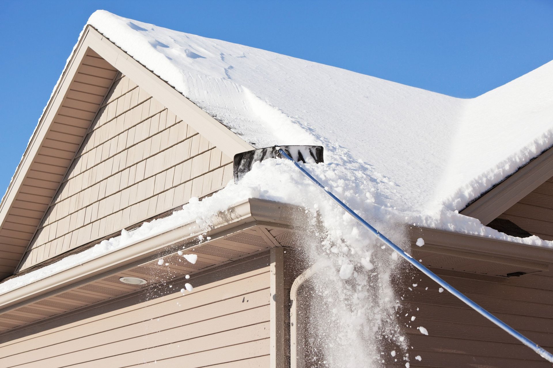 A person is raking snow off the roof of a house