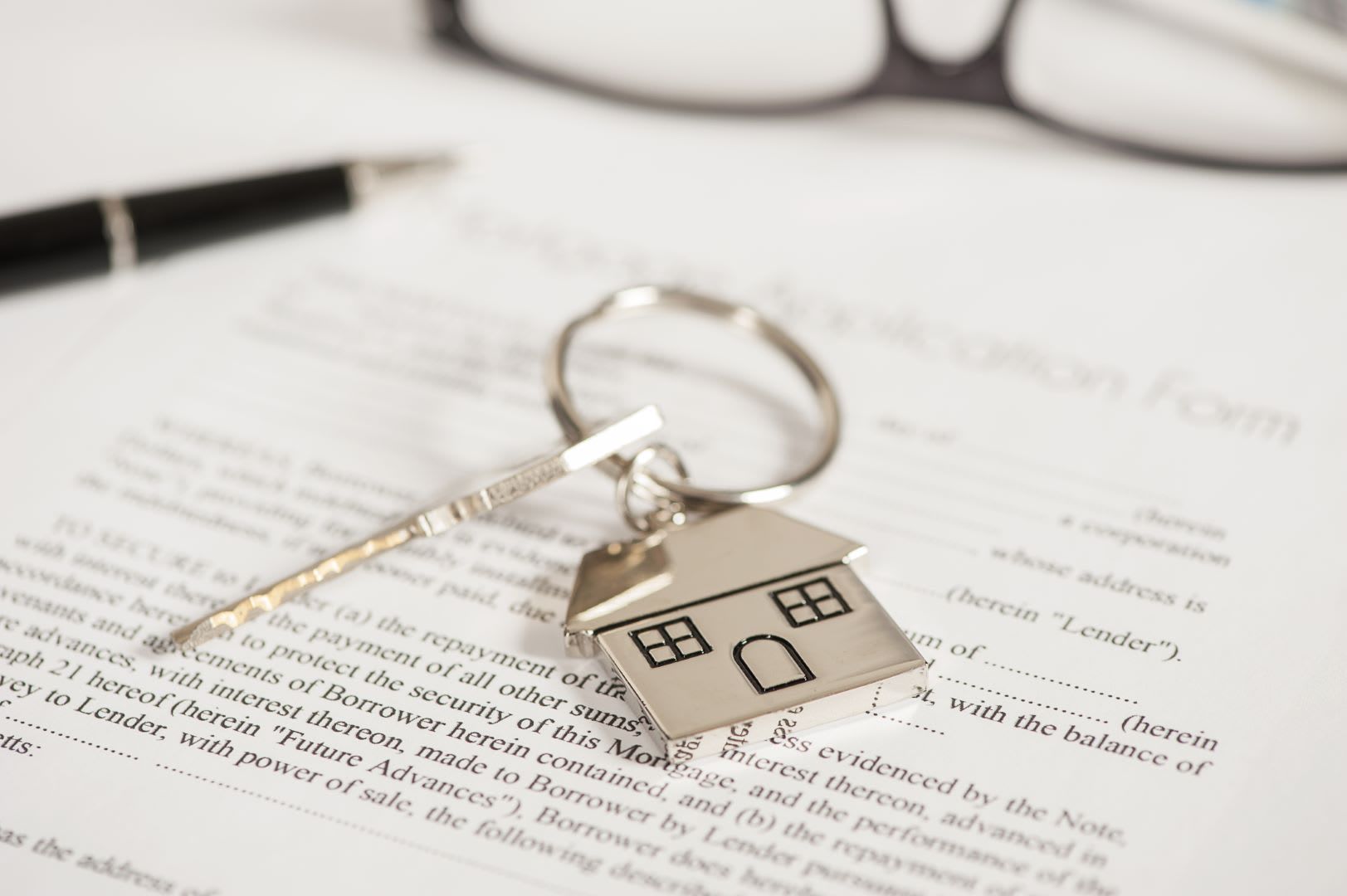 House key on a keyring, resting on a document with a pen and glasses in the background.