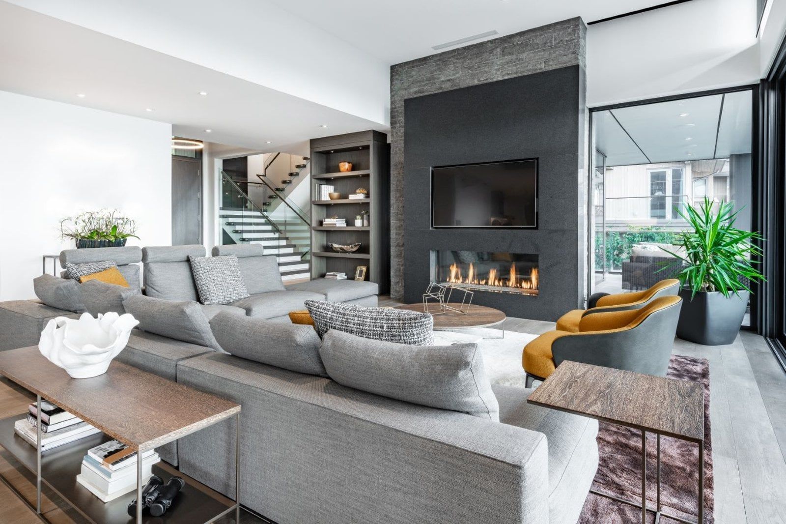 Modern living room with gray sectional sofa, fireplace, and staircase.