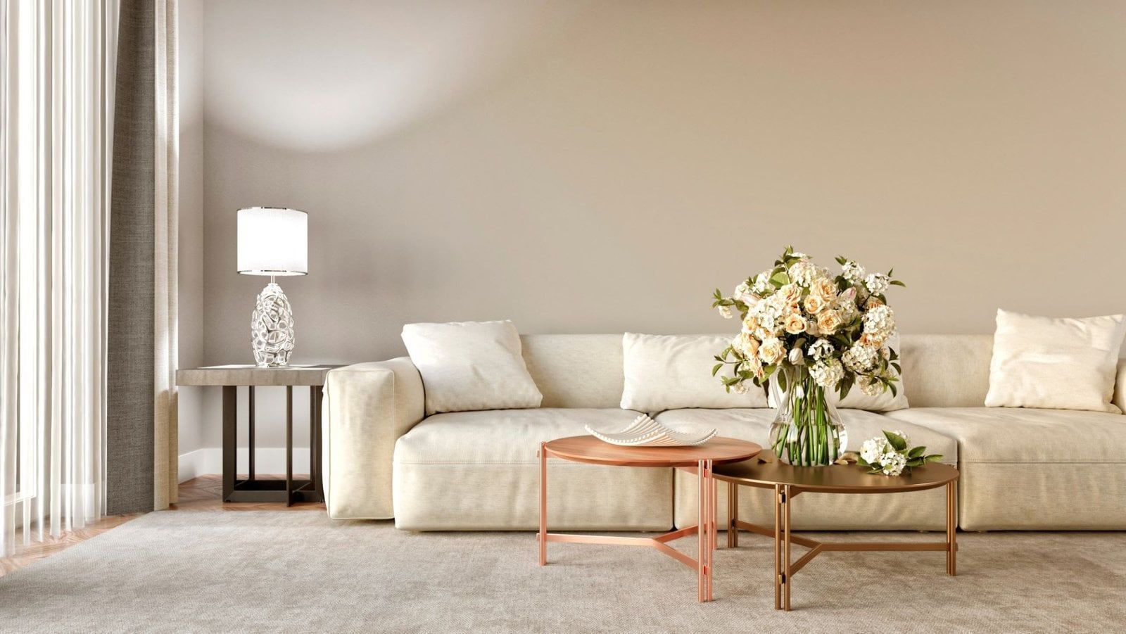 Living room with beige sofa, flowers, two round coffee tables, lamp, and neutral color wall.
