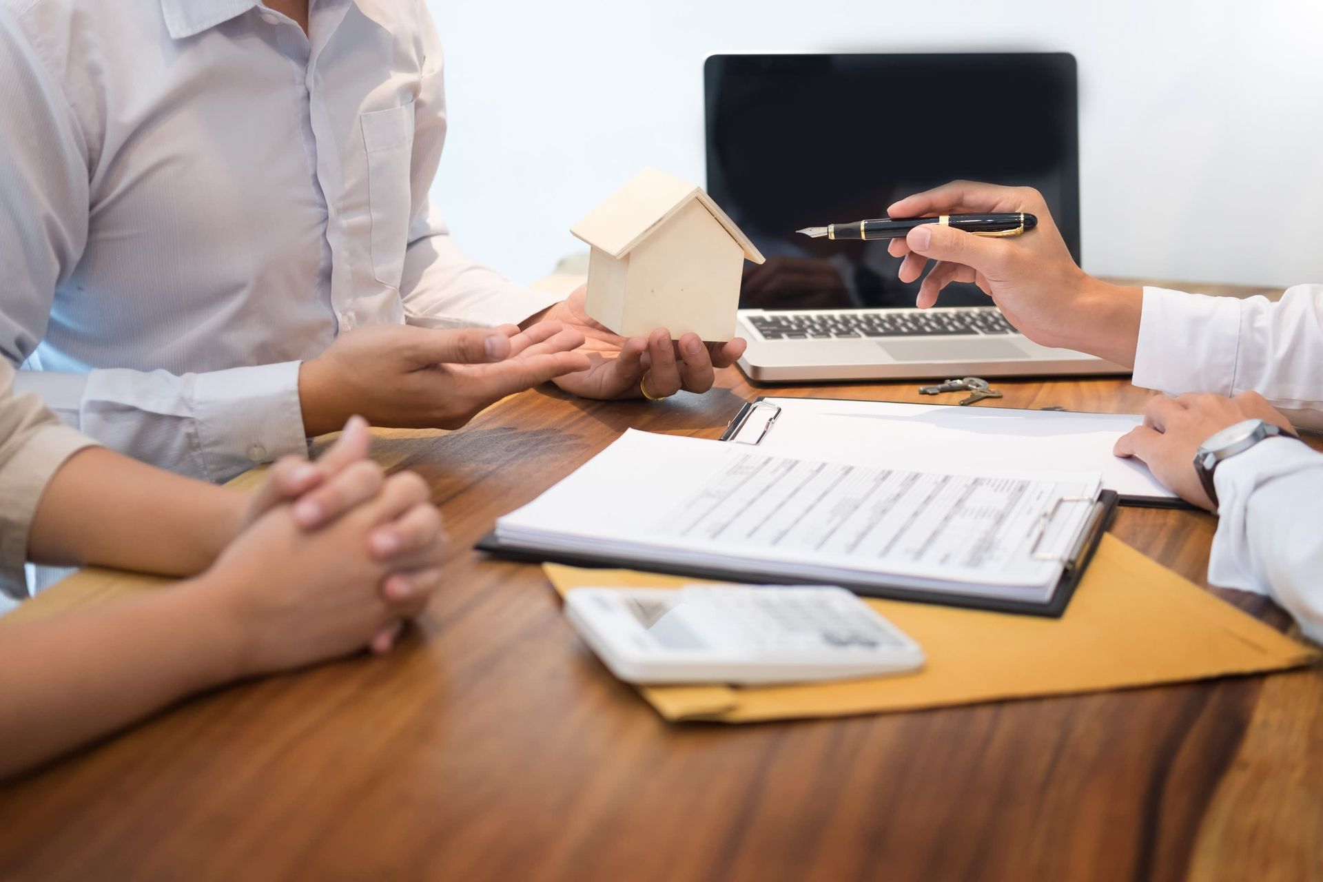 Two people reviewing paperwork with a realtor holding a model house.