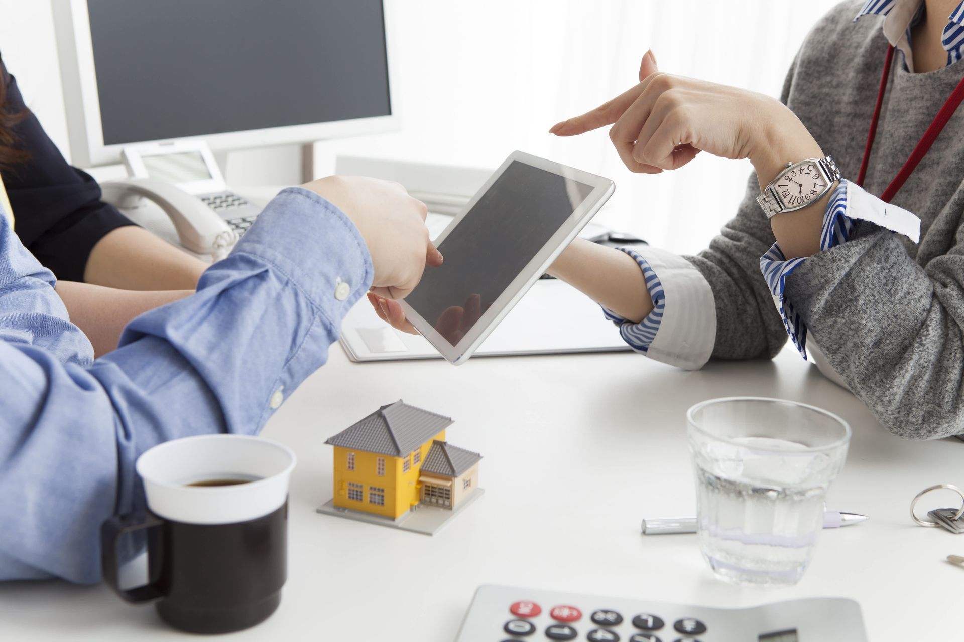 People at a desk, looking at a tablet. A small house model and coffee cup are on the desk.