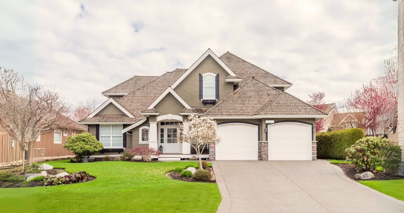 Two-story house with green lawn, driveway, and two-car garage. Overcast sky.