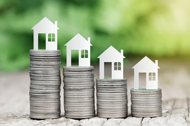 Stacks of coins with paper house cutouts on top, decreasing in height. Green background.
