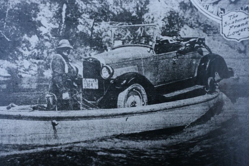 a black and white photo of a boat carrying an old vehicle