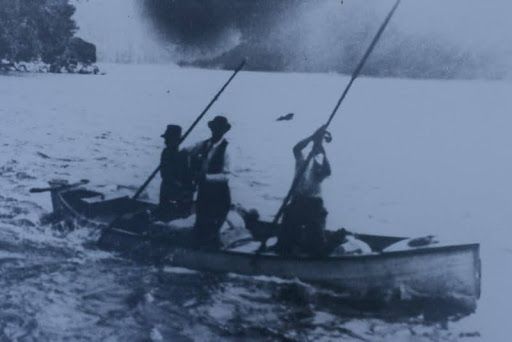 a black and white photo of three men in a canoe in the river