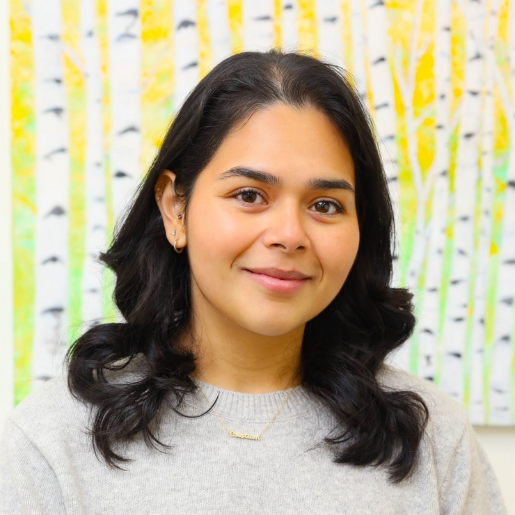 Woman in gray sweater smiles in front of a painting with yellow, white, and green birch trees.