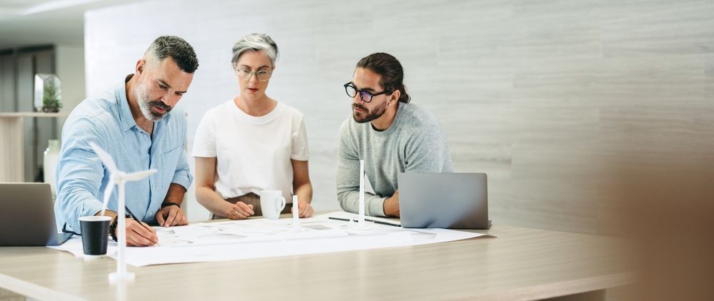 a group of people are sitting around a table looking at a blueprint.