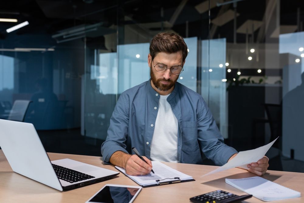 A man is sitting at a table with a laptop and papers.