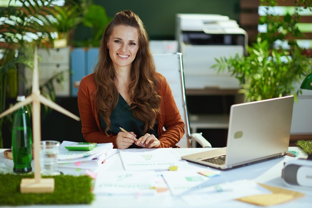 a woman is sitting at a desk with a laptop and a windmill in the background.