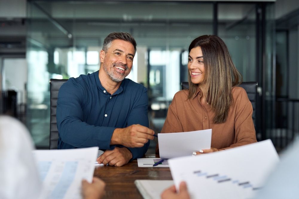 A man and a woman are sitting at a table with papers reviewing a document discussing high net worth individuals tax strategies.