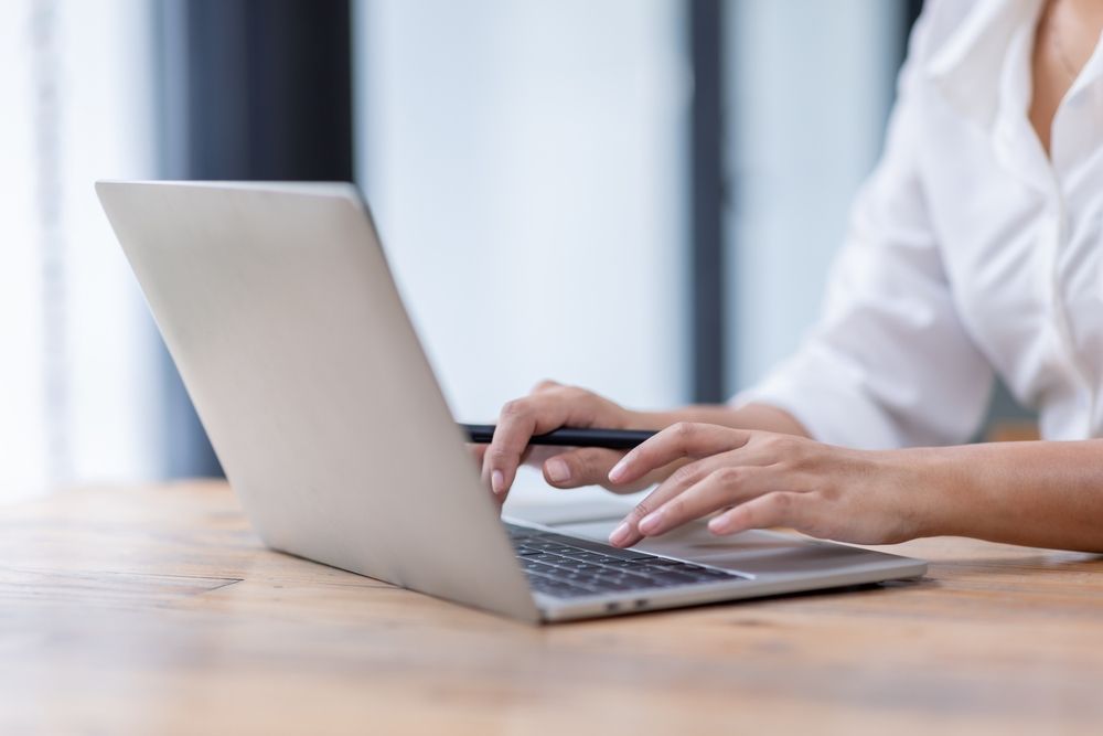 A woman is typing on a laptop computer while sitting at a table.