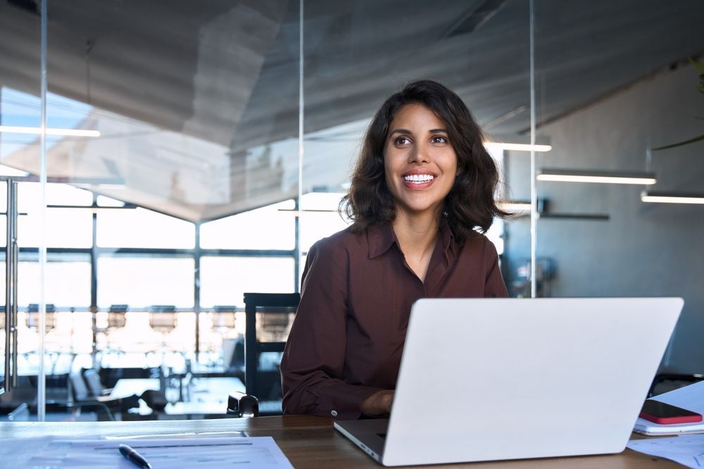 A woman is sitting at a desk in front of a laptop computer.