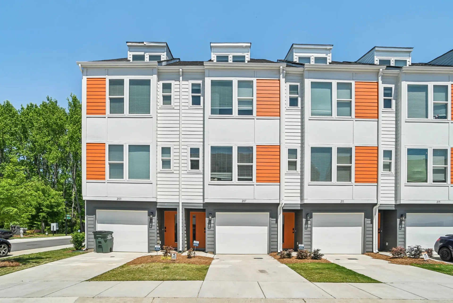 Row of modern white townhouses with orange accents and attached garages.