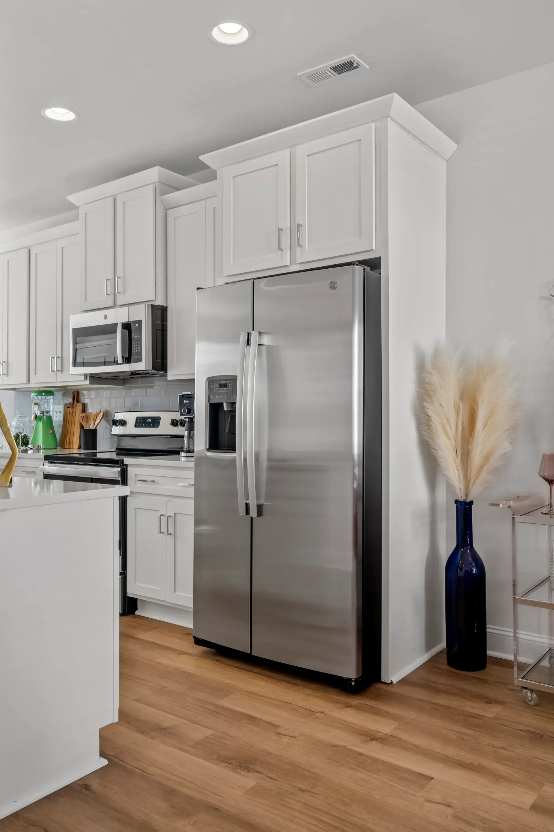Bright kitchen with white cabinets, stainless steel refrigerator, and wooden floors.