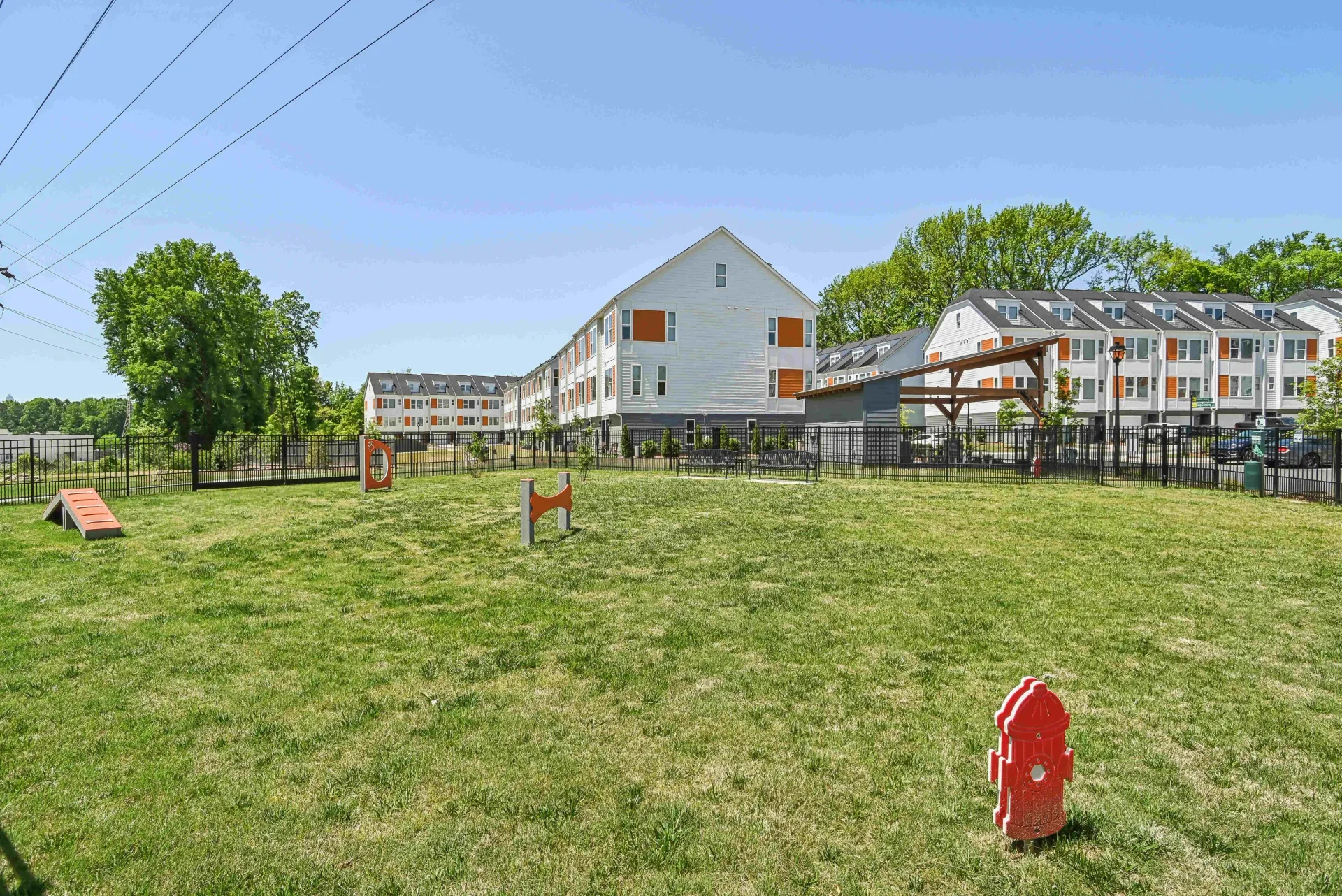 Green grass yard with apartment buildings in the background. Orange accents on the building. Clear, sunny sky.