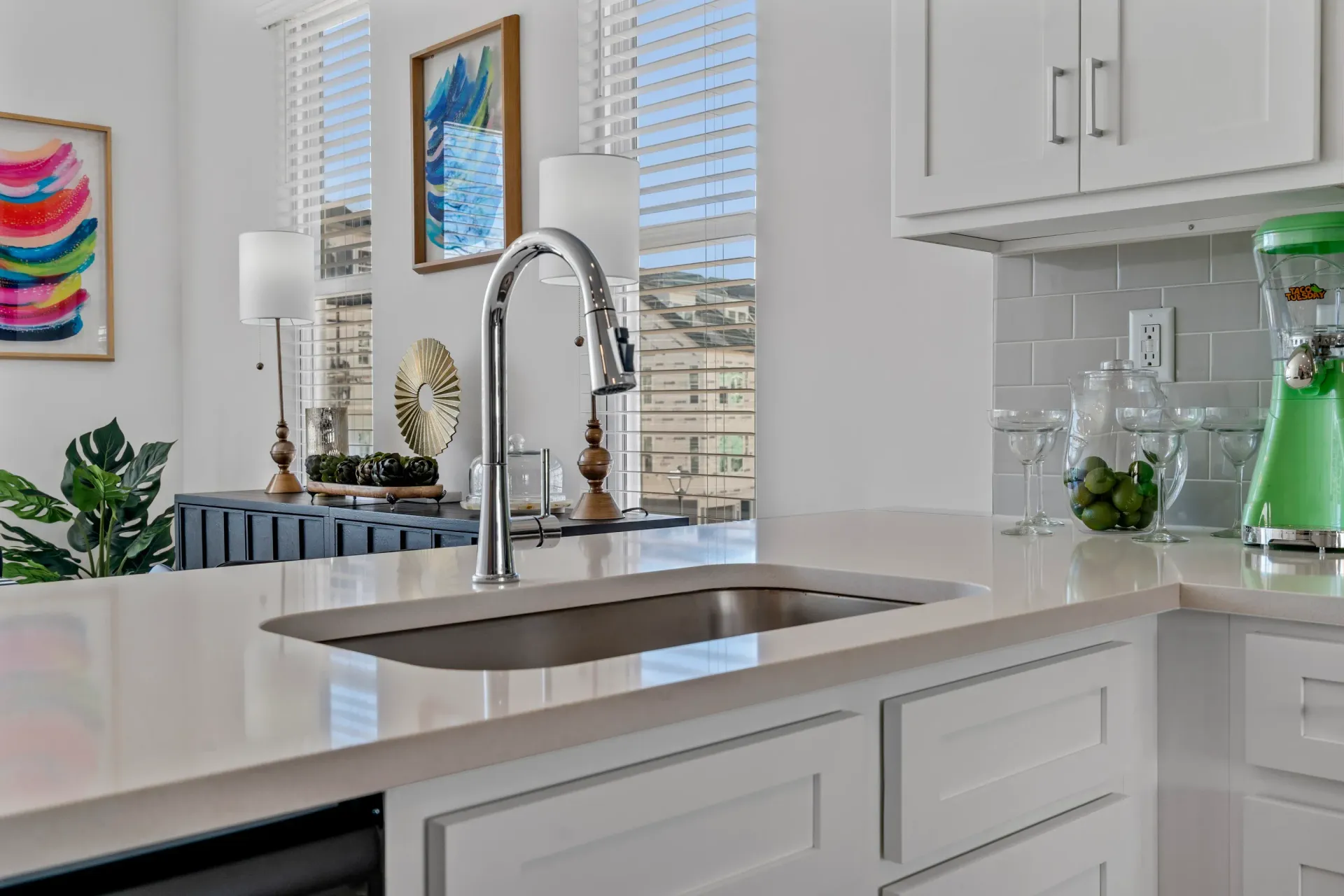 White kitchen with a sink, faucet, and counter, and a colorful abstract painting.