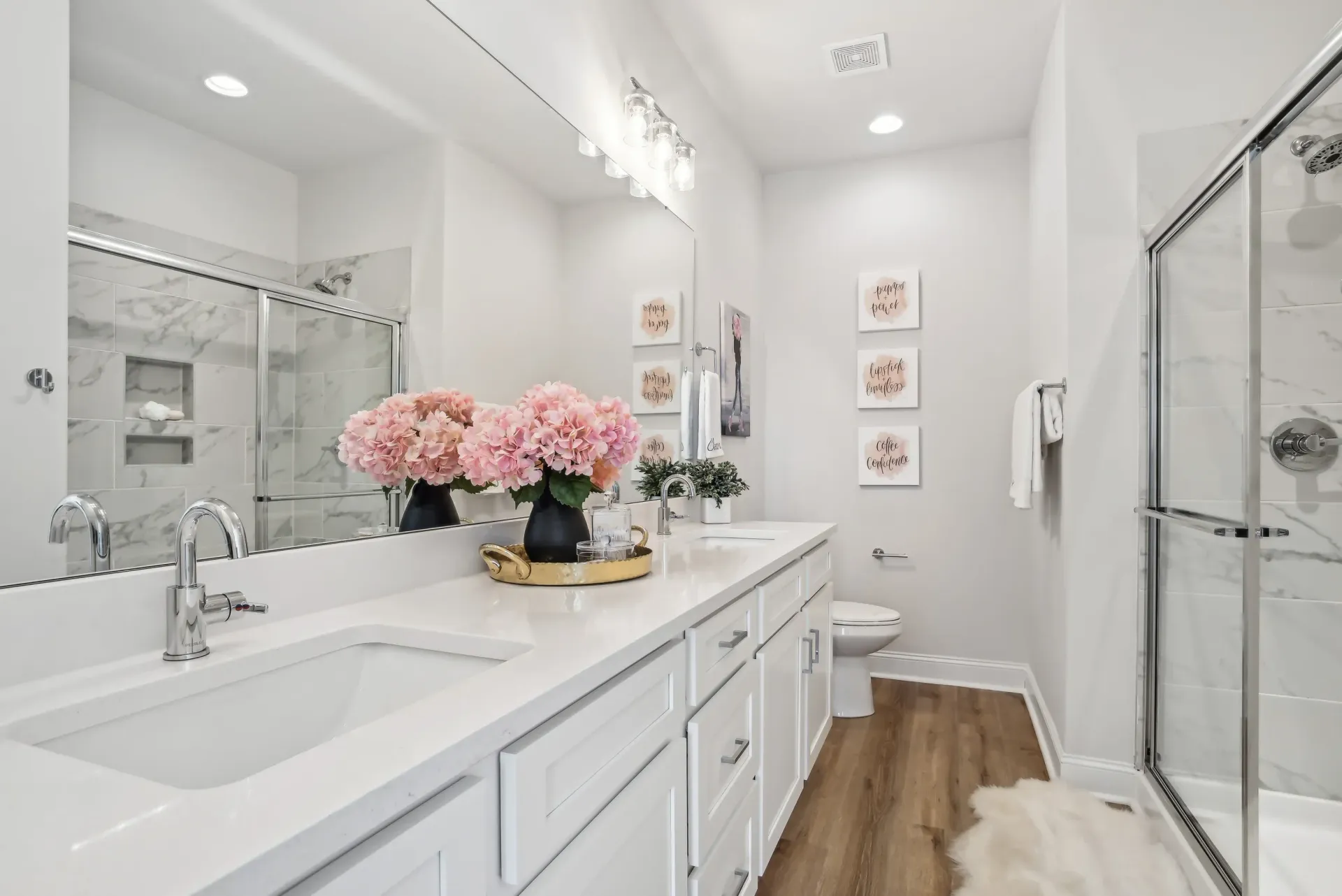 Bright bathroom with white double vanity, marble shower, and pink hydrangea bouquets.