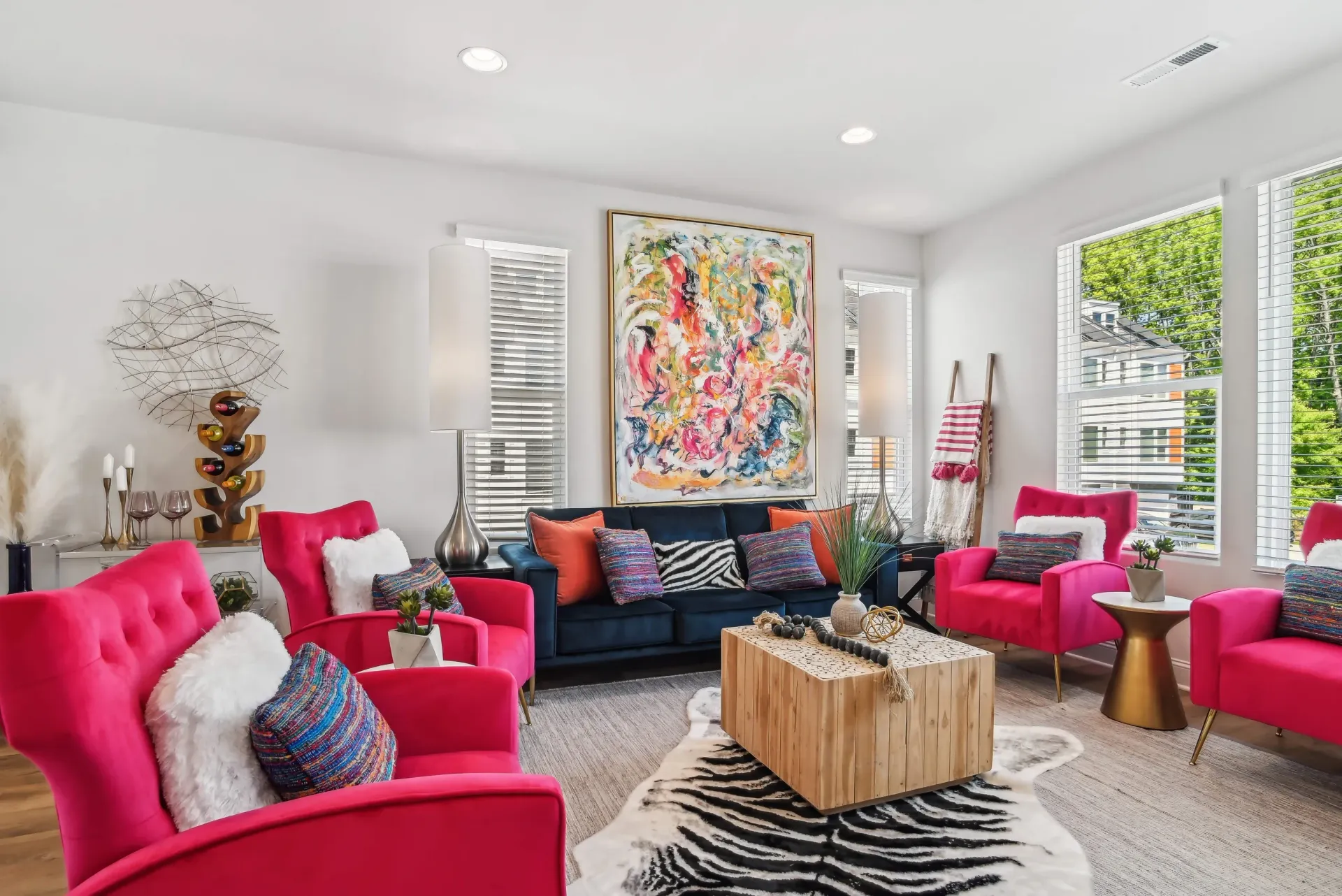 Bright apartment living room with large windows, pink accent chairs, navy sofa, and abstract artwork.