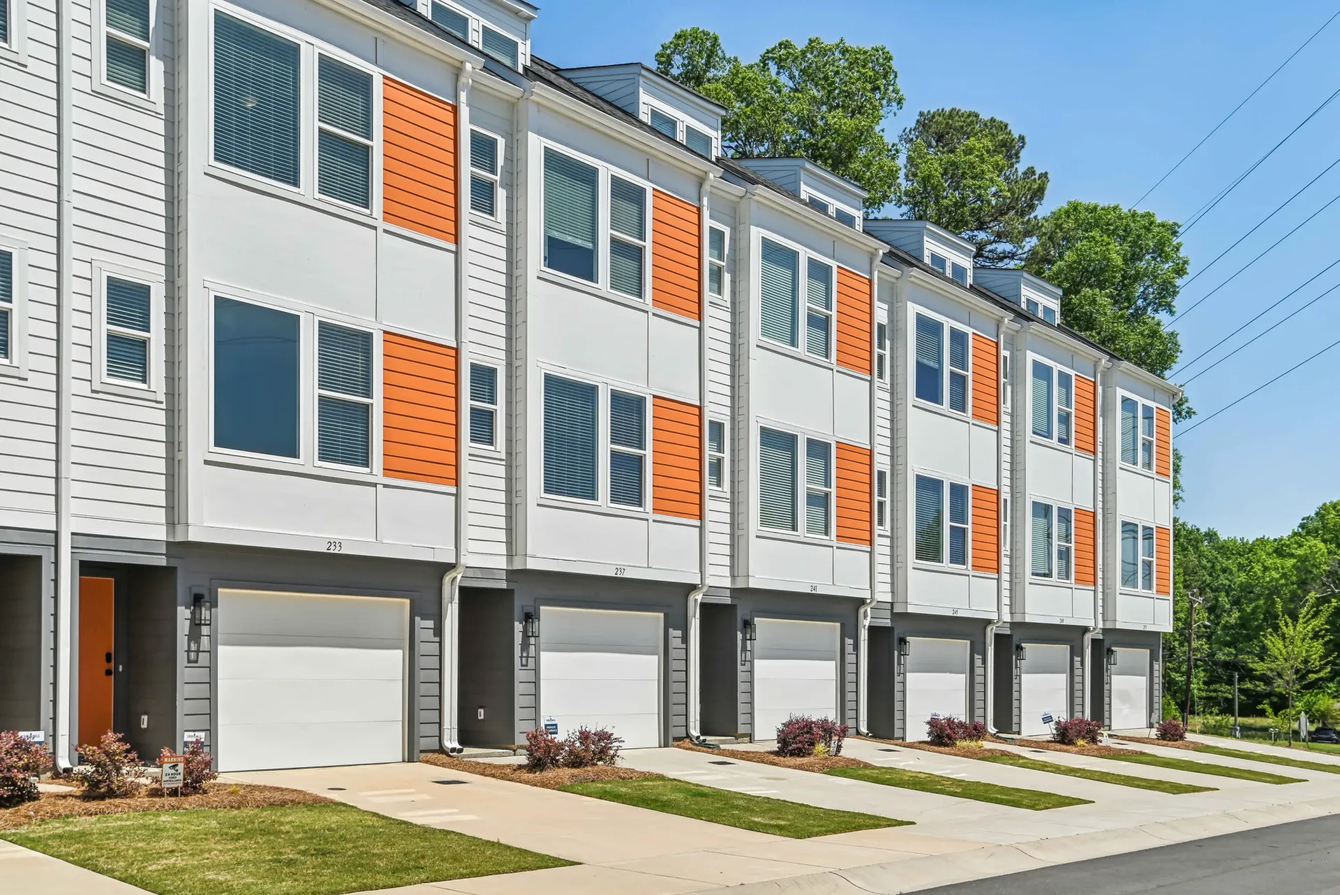 Row of modern townhome buildings with attached garages and orange accent panels.