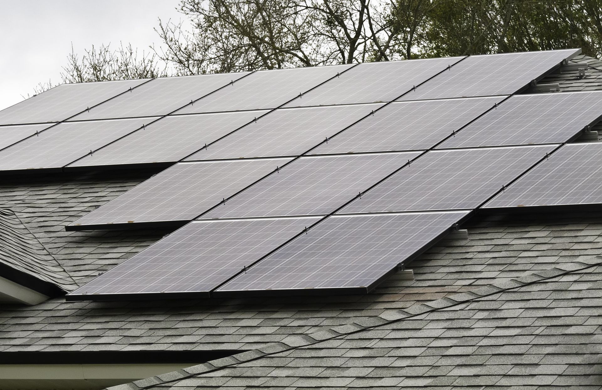 Solar panels installed on a shingled roof under an overcast sky