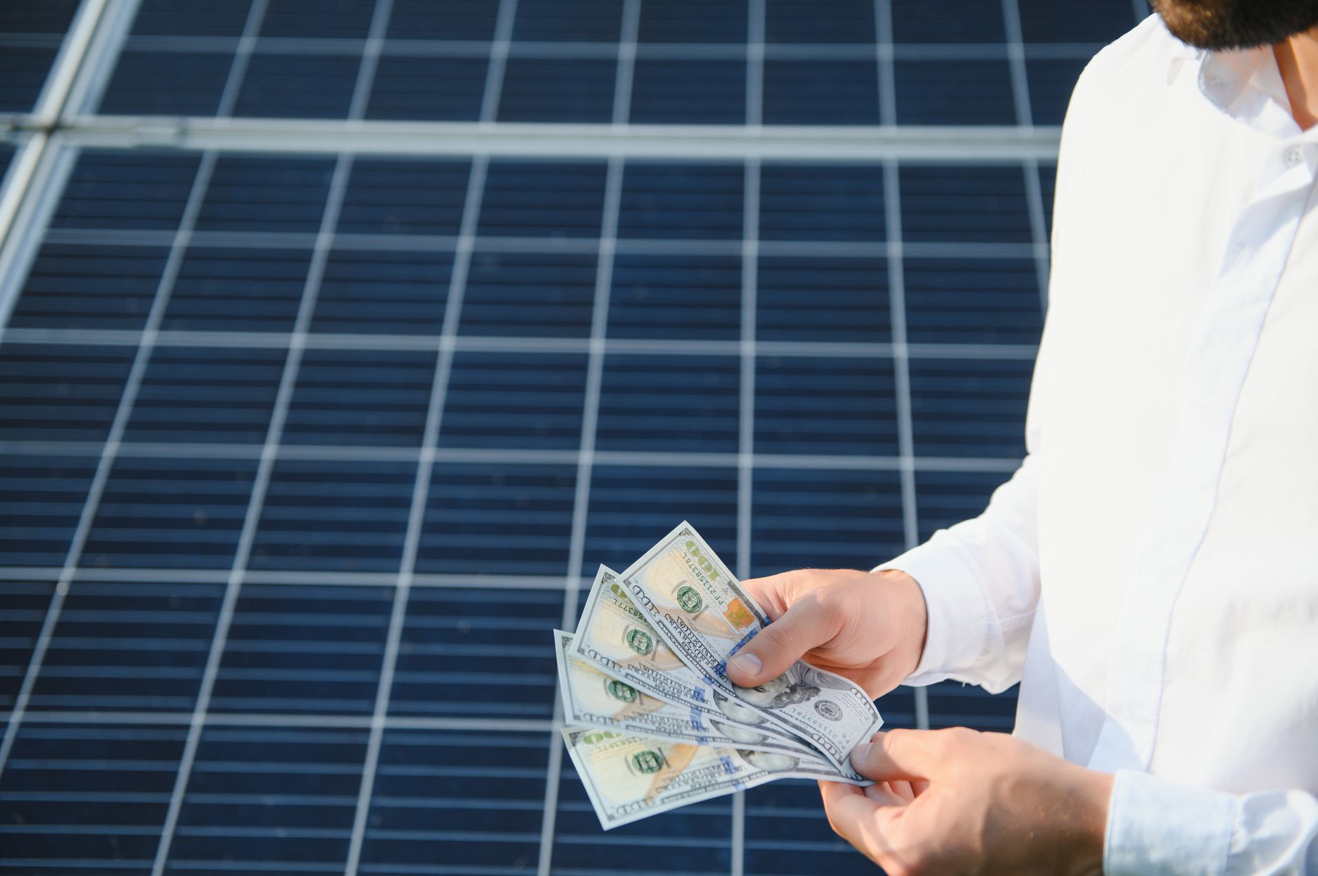 Man in white shirt counting cash in front of solar panels
