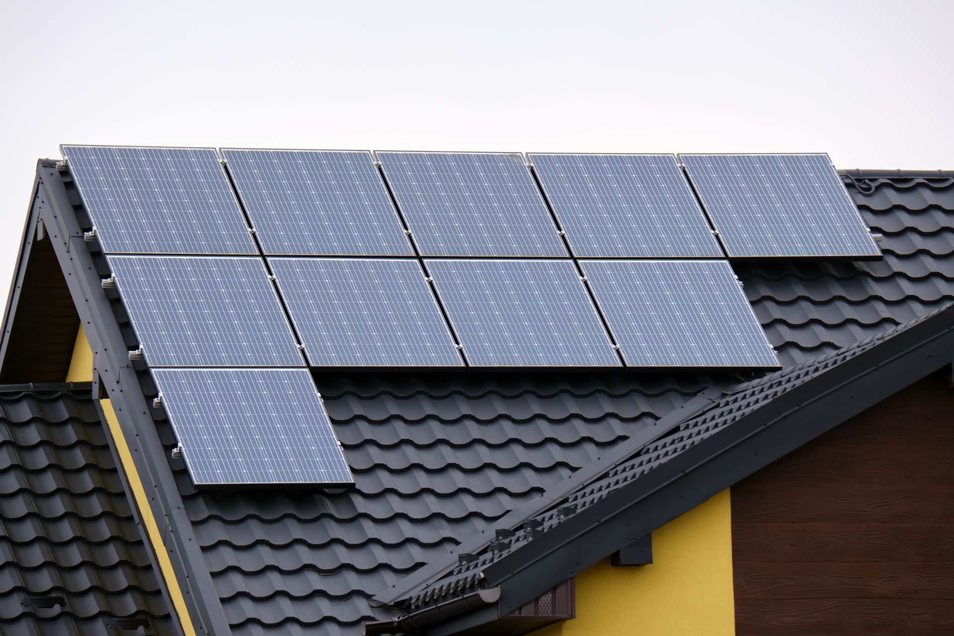 Solar panels mounted on a dark tiled roof with a yellow house wall visible.