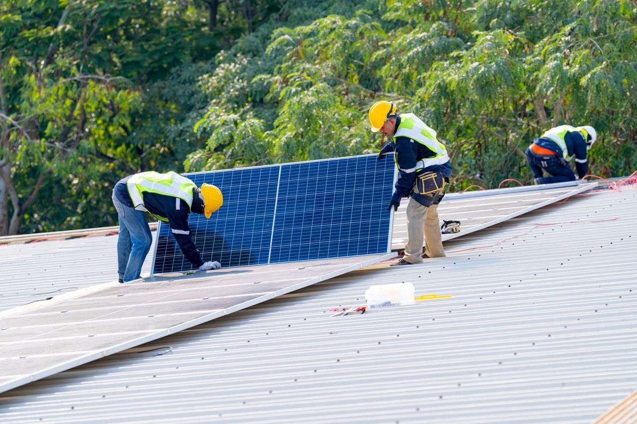 Workers installing solar panels on a metal roof, with trees in the background