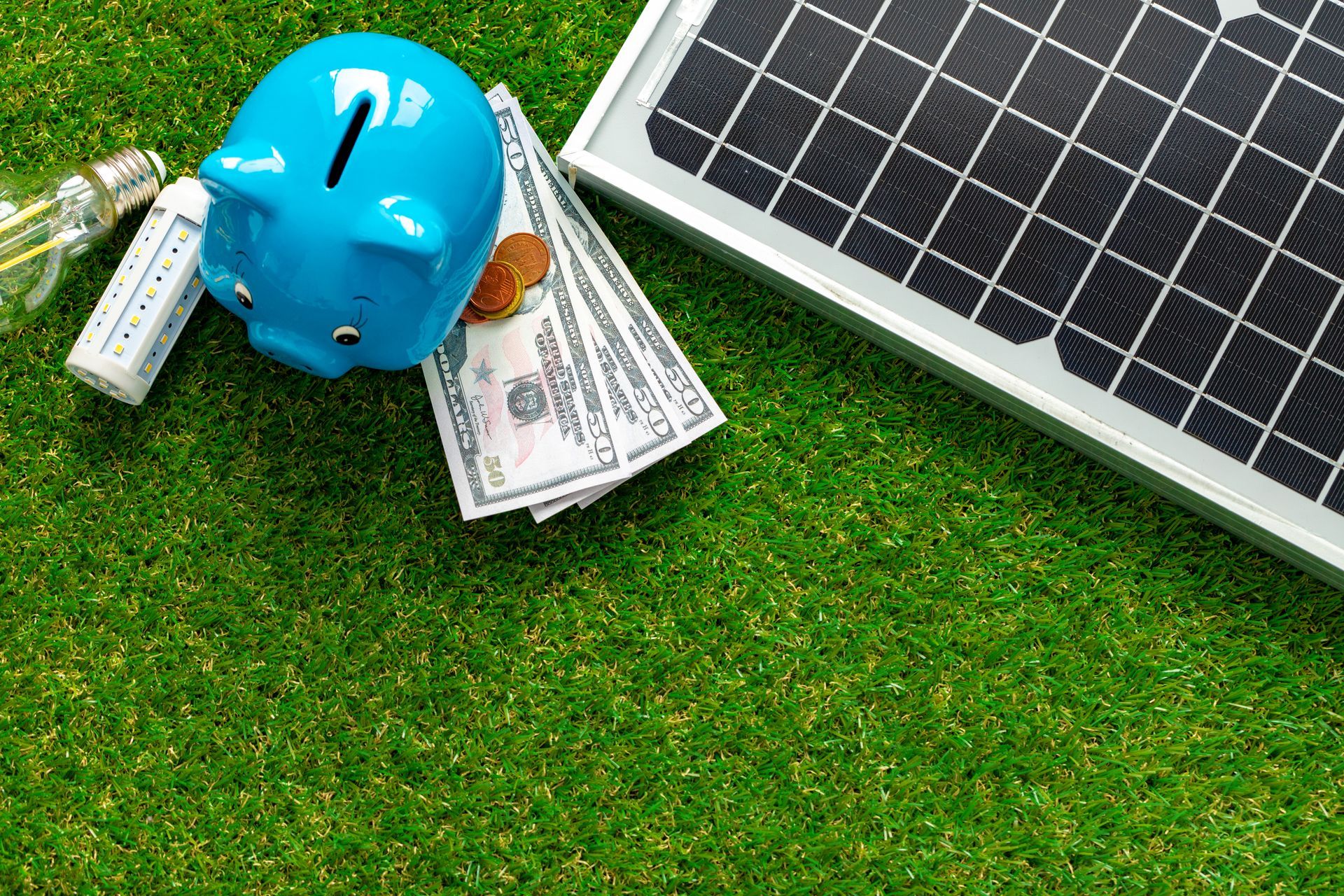 Solar panel beside blue hard hat and cash on grass, symbolizing renewable energy savings
