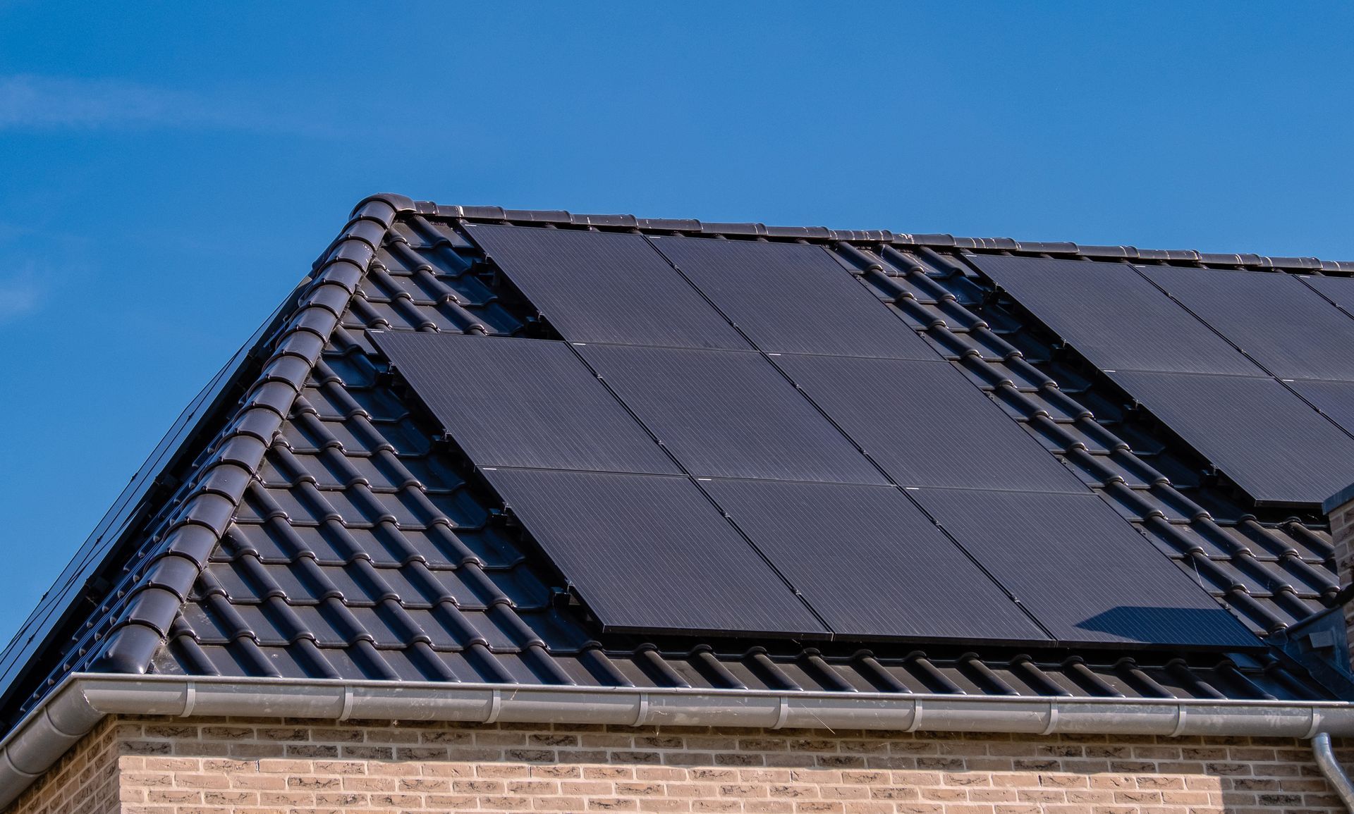 Roof with dark solar panels on a tiled house against a blue sky