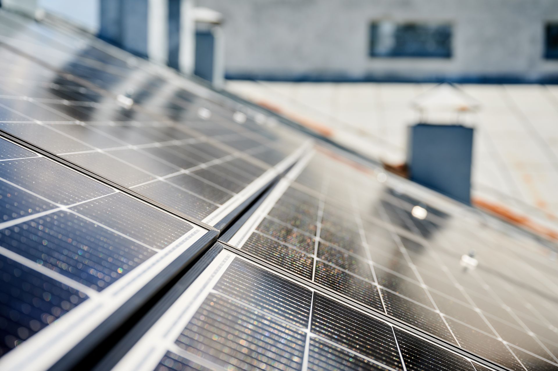 Solar panels angled on a rooftop, reflecting sunlight against a blurred urban background