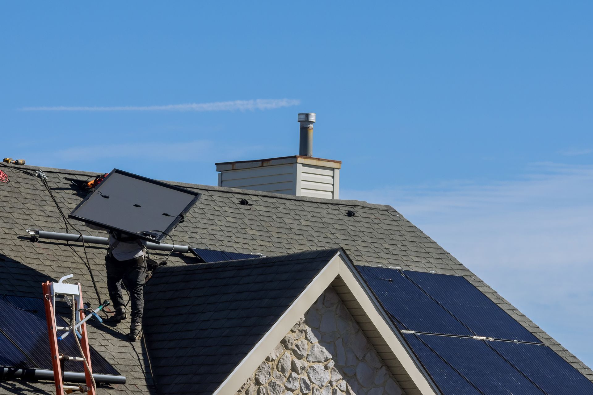 Solar panels and a rooftop antenna on a house under a clear blue sky